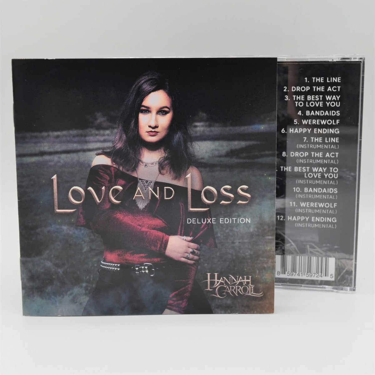 Love and Loss CD cover showing Hannah Carroll standing in green grass. CD back partially appears behind CD front, revealing 12-track song list.